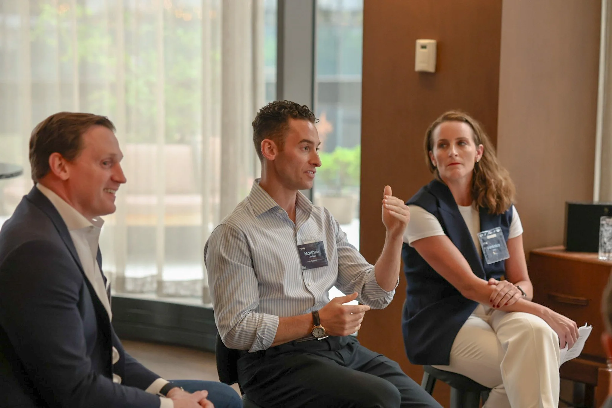 Four people sitting in a row at a panel discussion or meeting, one man speaking and gesturing with his hand, others listening.