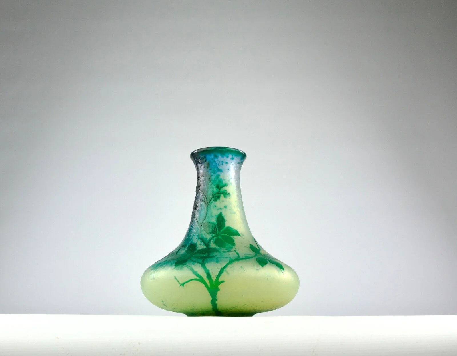 A glass vase with a decorative green plant pattern, set against a neutral background.