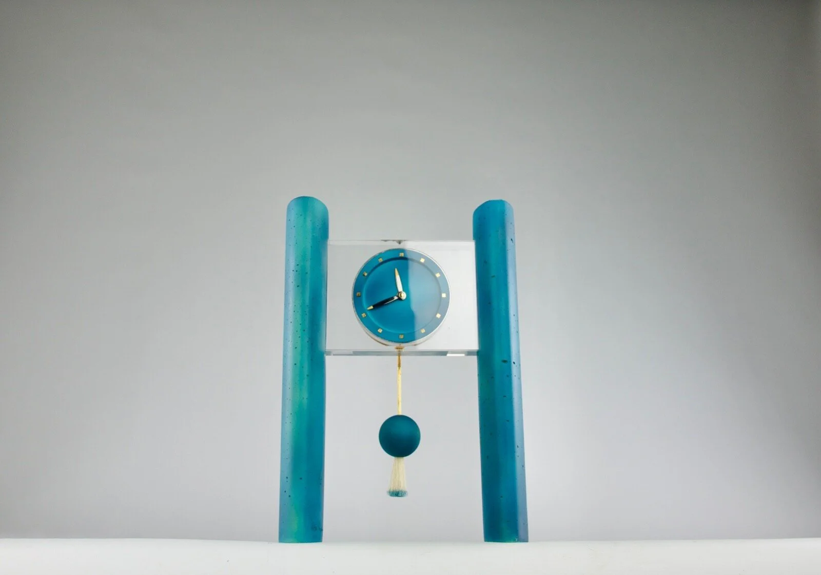 A modern blue clock with a pendulum on a white background.
