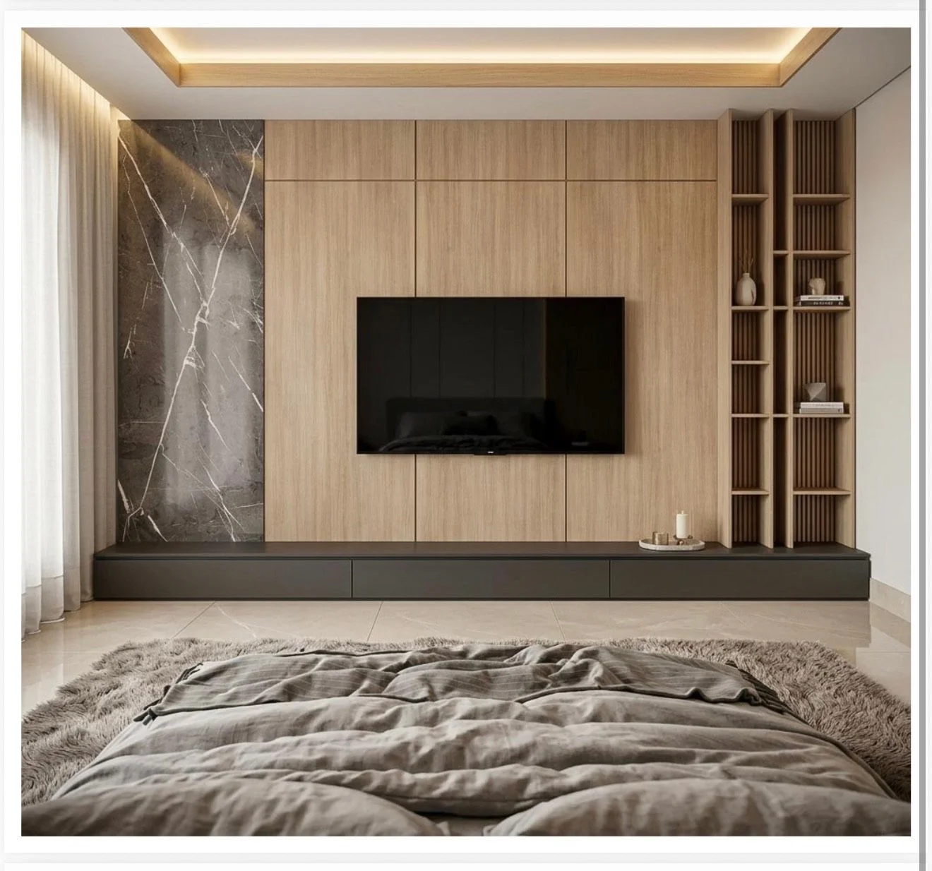 Modern bedroom with a large flat-screen TV mounted on a wooden-paneled wall, a built-in shelving unit with decorative items, and a bed with a plush blanket in the foreground. The room has a neutral color scheme with natural light coming through sheer