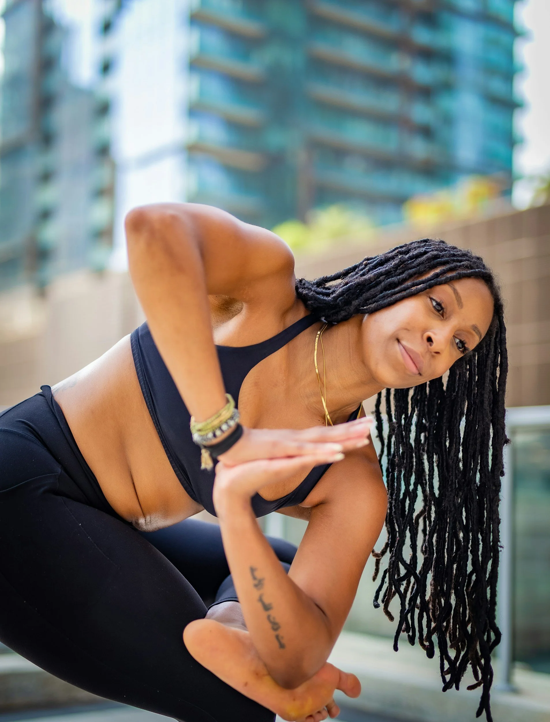A woman with long dreadlocks taking a selfie outdoors on a city street, wearing a sports bra and leggings.