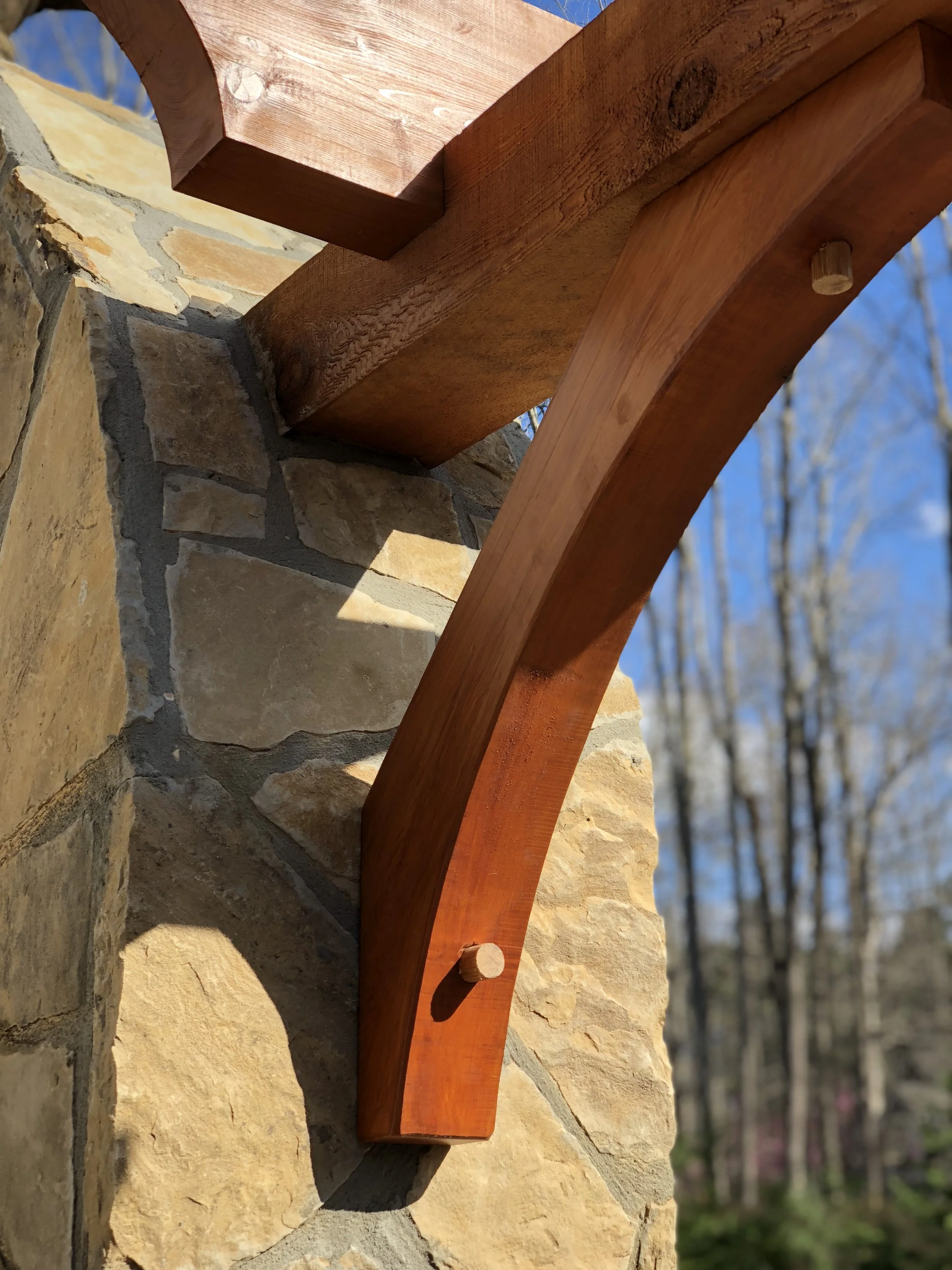 Close-up view of a wooden bracket attached to a stone wall, with clear blue sky and blurred trees in the background.