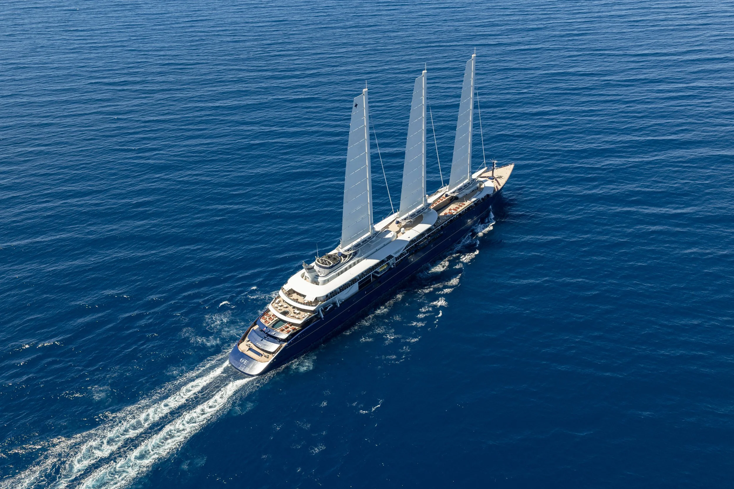 A large luxury sailboat with multiple decks and tall masts sailing on the open ocean.