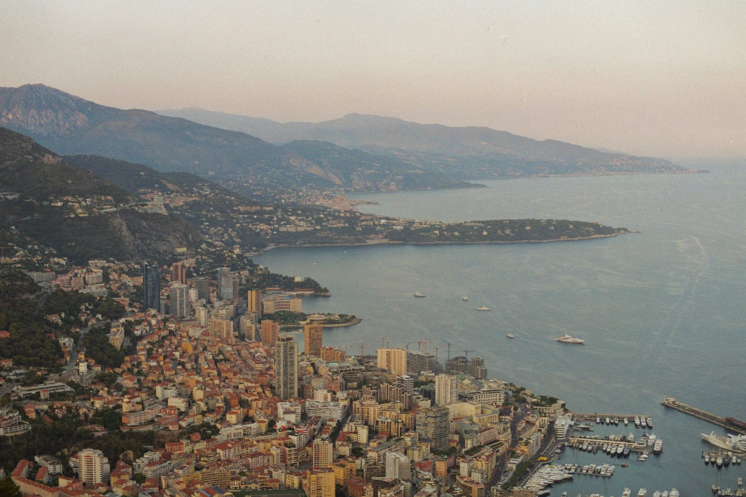 Aerial view of a city with high-rise buildings, hills, and a waterfront with boats and a marina.