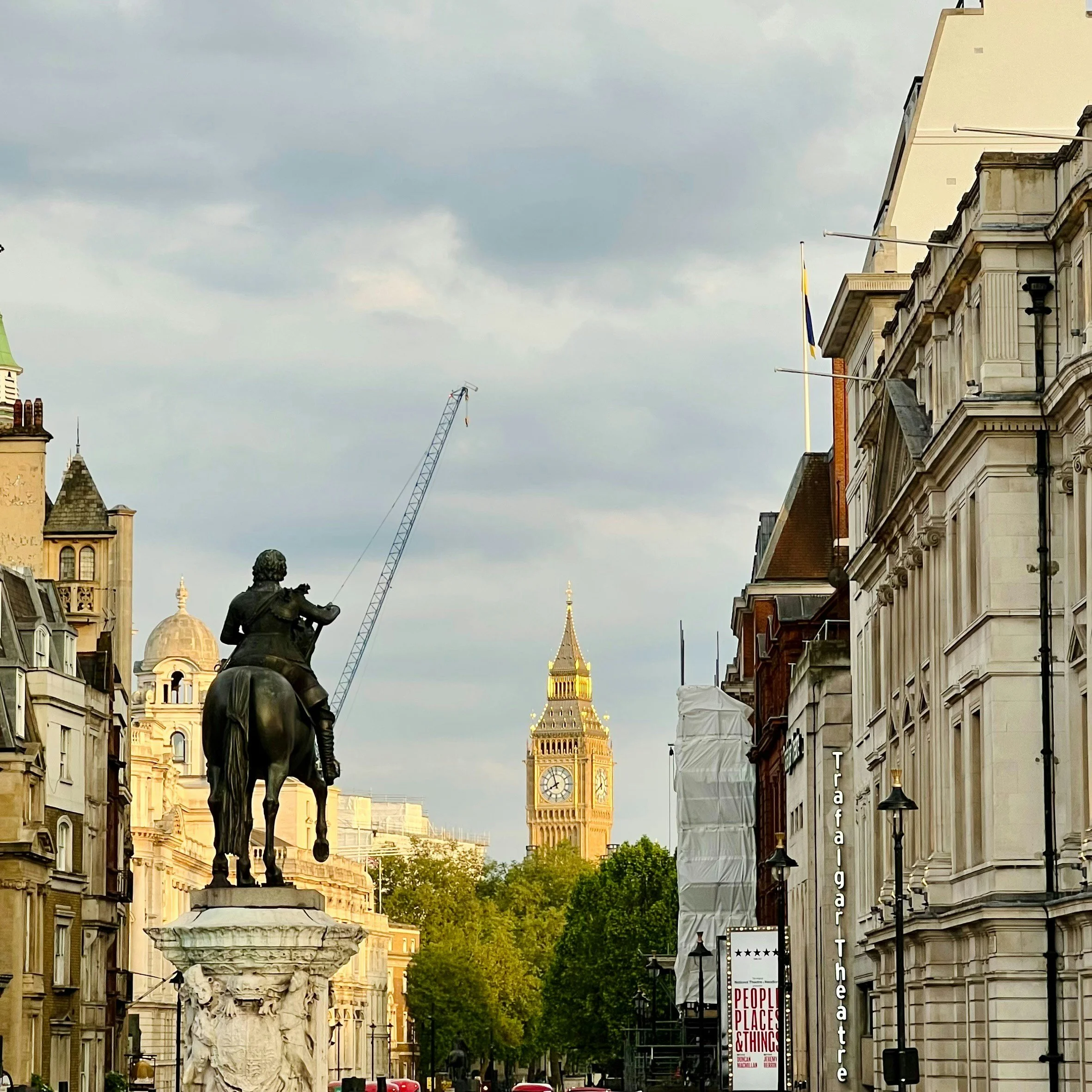 A city street scene with historic buildings, a statue of a man on a horse, a crane in the background, and Big Ben in the distance.