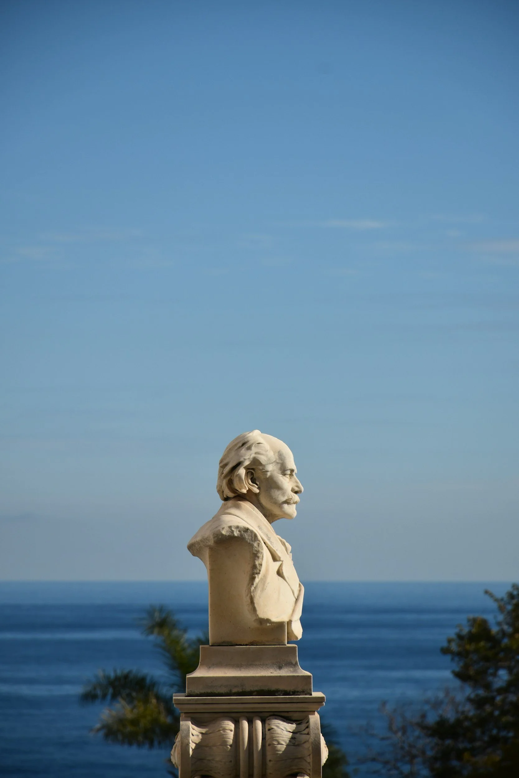 Marble bust of Abraham Lincoln on a decorative pedestal, with a clear blue sky, ocean, and palm trees in the background.