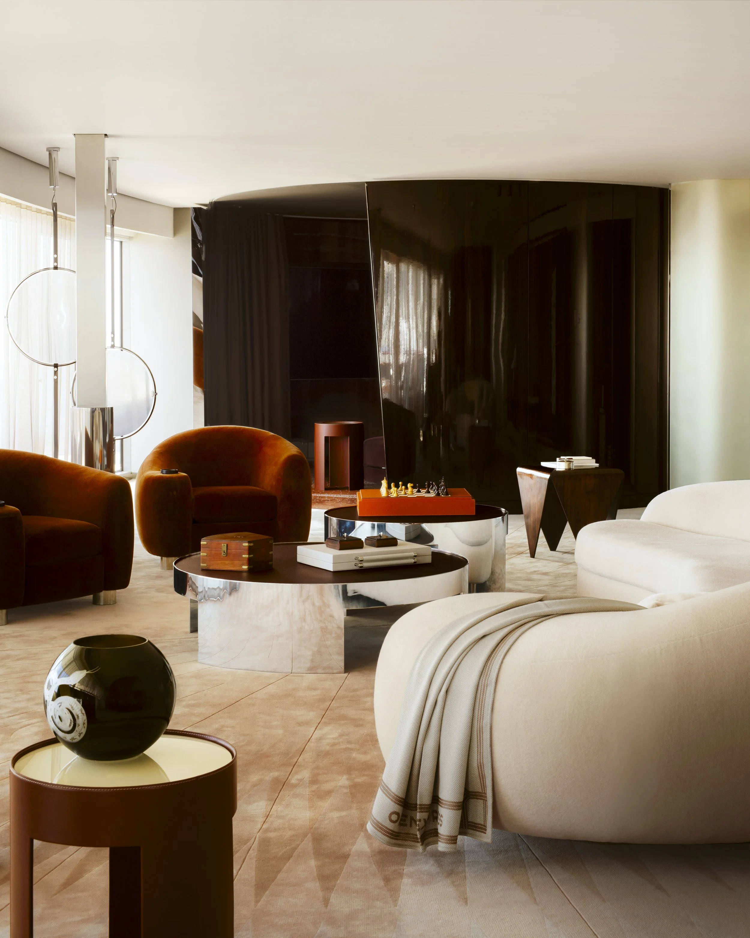 Contemporary living room with plush beige and burnt orange chairs, black and white accessories, modern lighting fixtures, and a large black curved decorative panel.