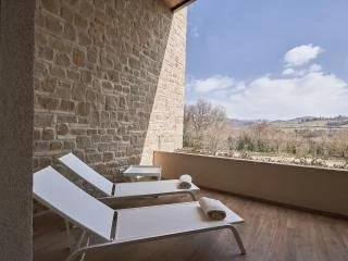 Two lounge chairs with rolled-up towels on a balcony overlooking a landscape with trees and hills.