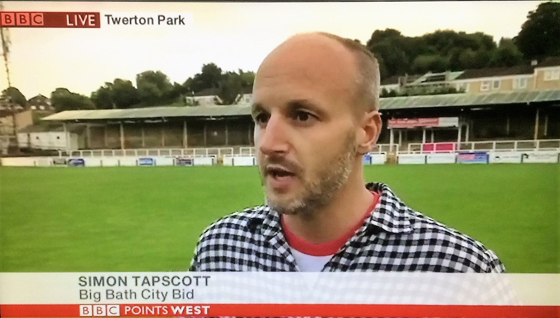 A man being interviewed on a football field with a stadium in the background. The caption shows his name as Simon Tapscott and mentions the Big Bath City Bid. The news segment is live from BBC Points West.