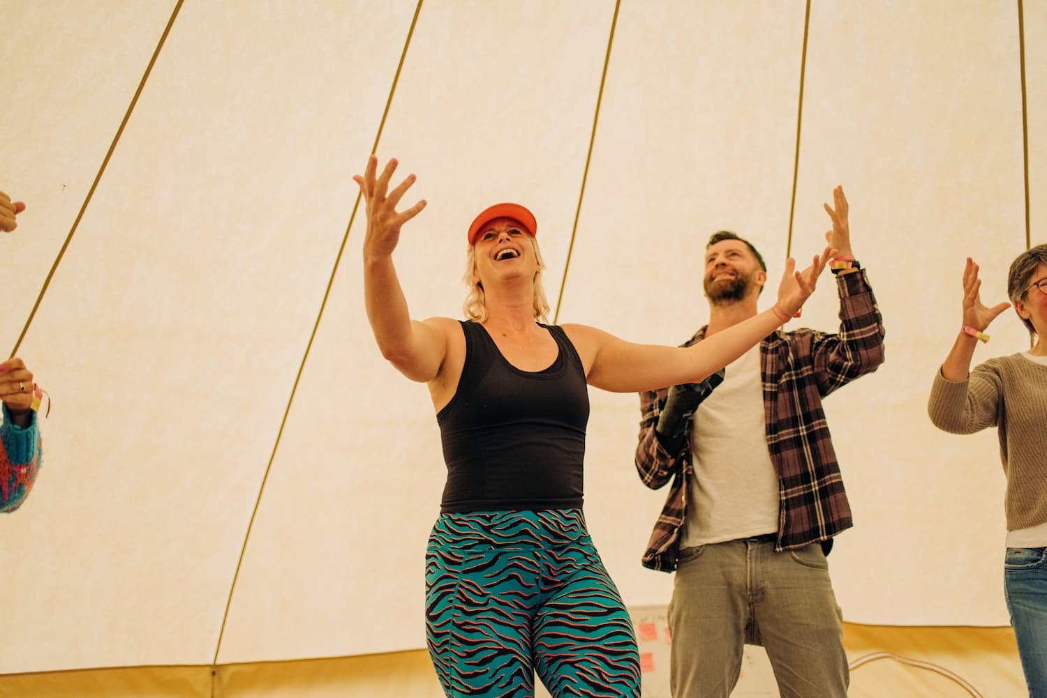 People dancing inside a tent with a beige interior, smiling and raising their arms, enjoying themselves.