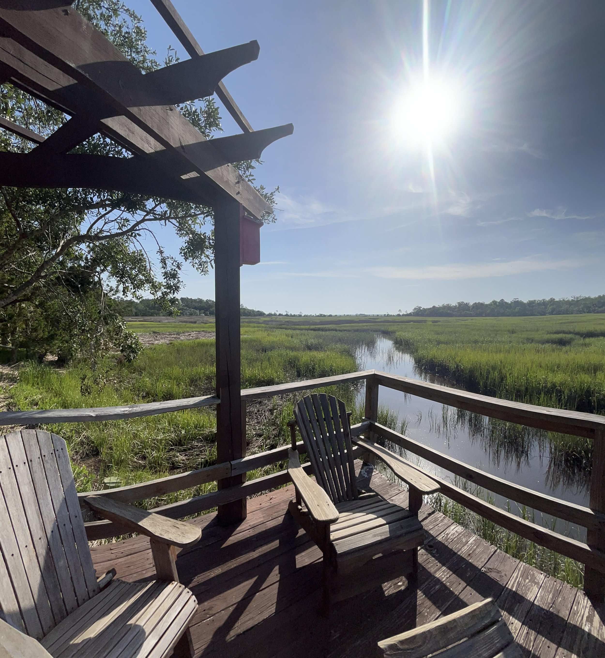 Adirondack chairs on deck near marsh with sun shining