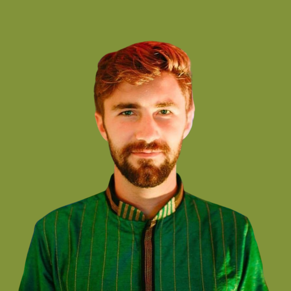 A young man with red hair and a beard wearing a green traditional jacket with vertical stripes, standing against a green background.