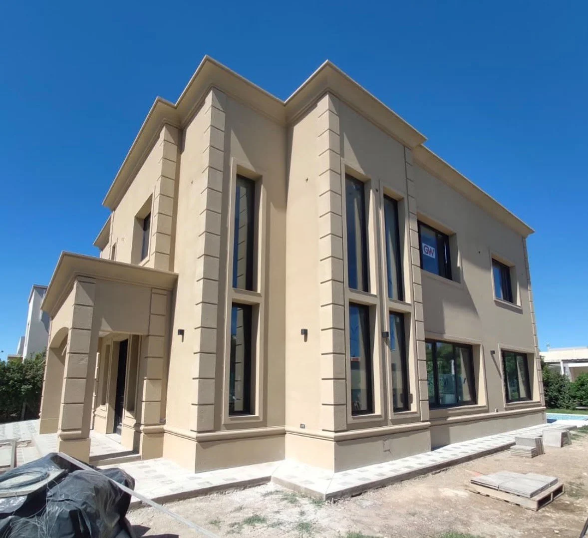 Newly constructed beige multi-story house with large windows, located on a sunny day.
