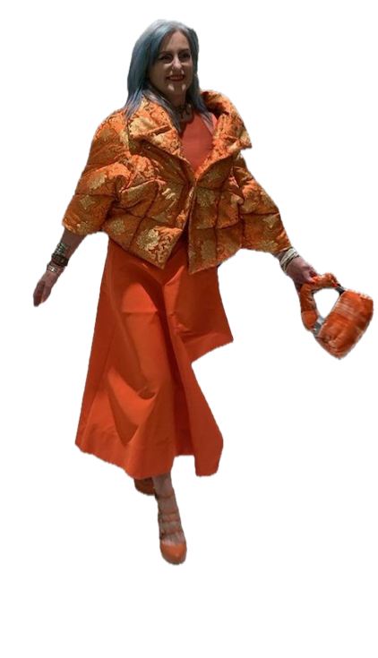 A woman with blue hair wearing an orange outfit consisting of a puffy jacket and a long skirt, carrying a small matching handbag, and smiling.