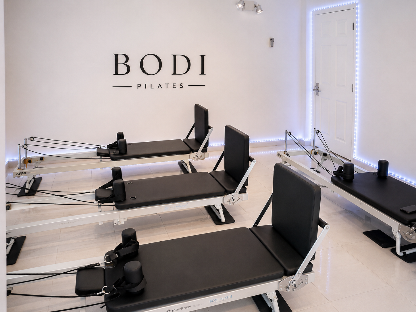 Pilates reformer machines in a pilates studio with white walls and a sign that reads "BODI PILATES."