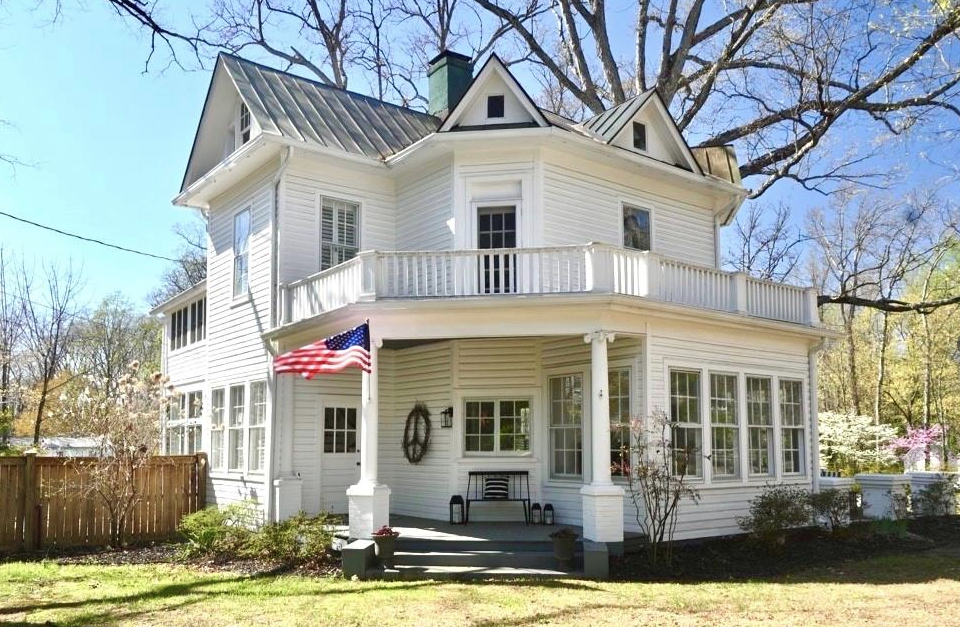 White Victorian house with a porch, multiple windows, and an American flag on the porch. Trees are in the background. Located in Bon Air, Virginia.