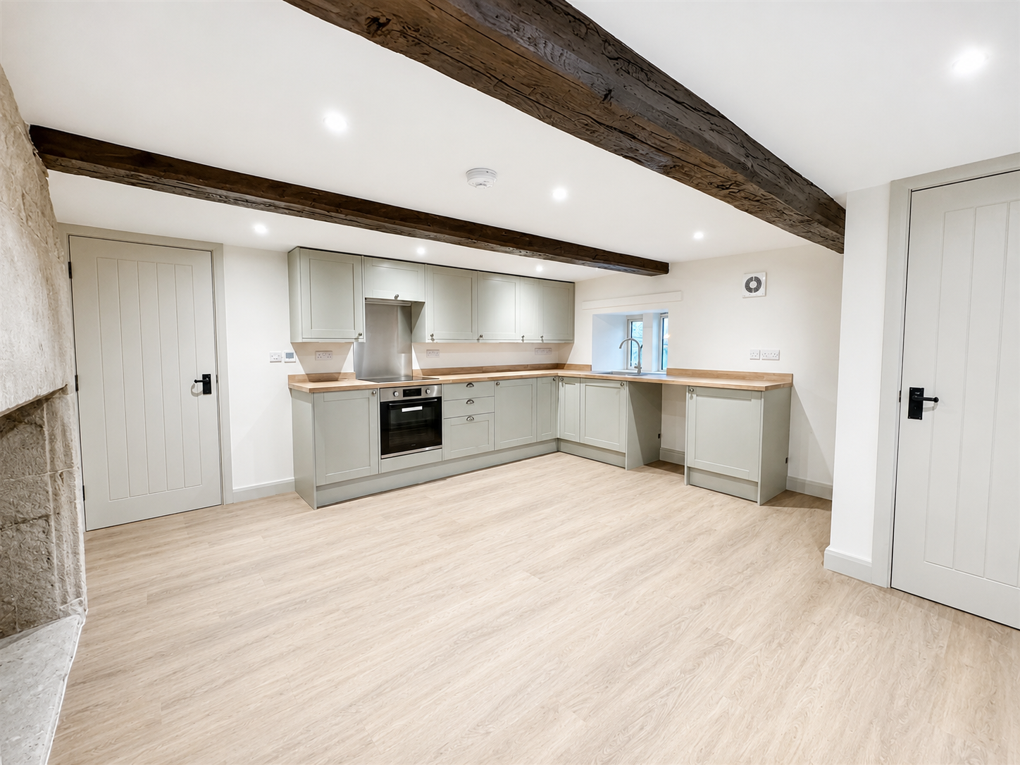 Renovated kitchen and living space featuring exposed timber beams and restored stone fireplace.