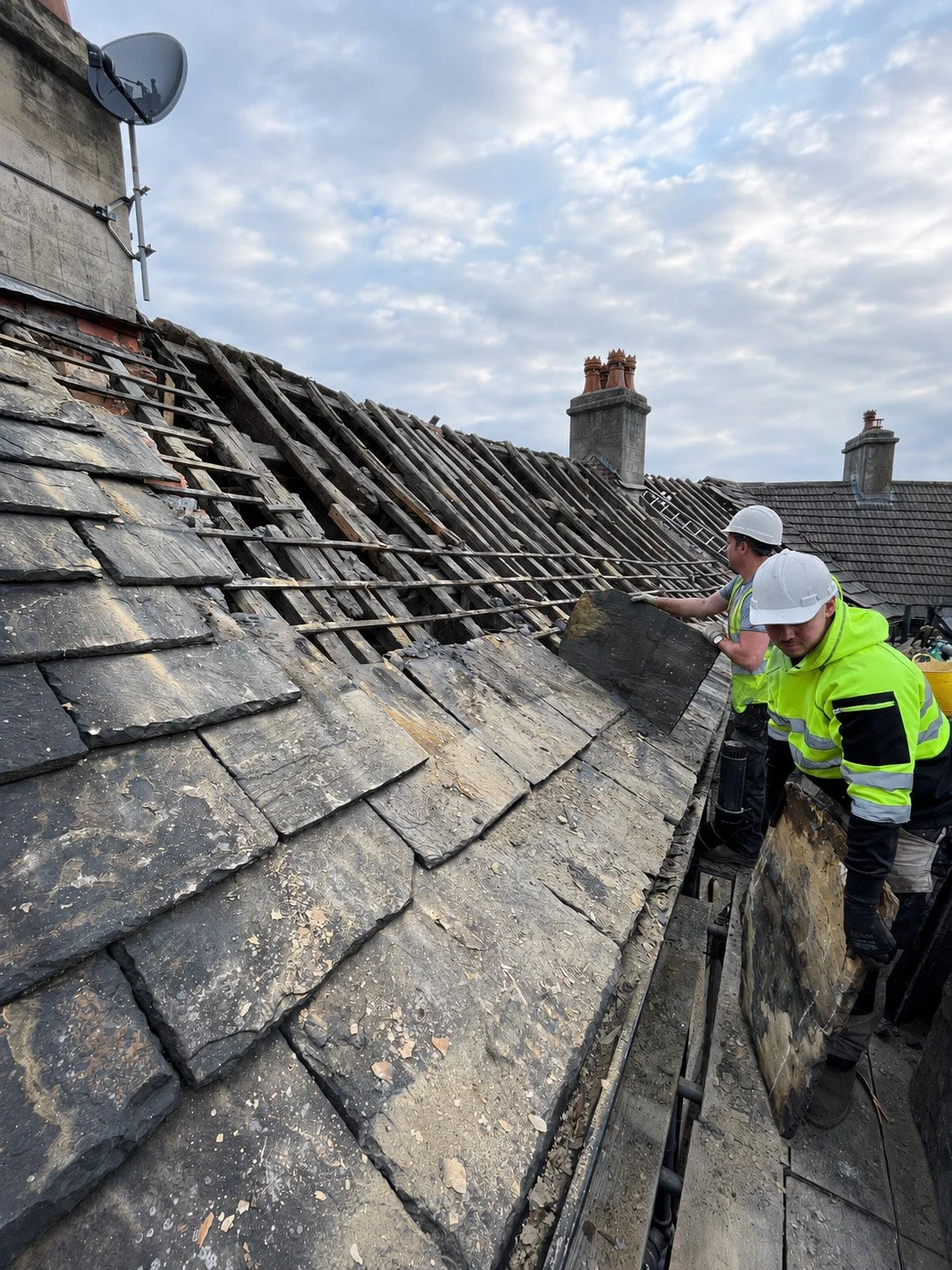 Builders carrying out roof restoration work on a traditional slate roof as part of a heritage renovation project.