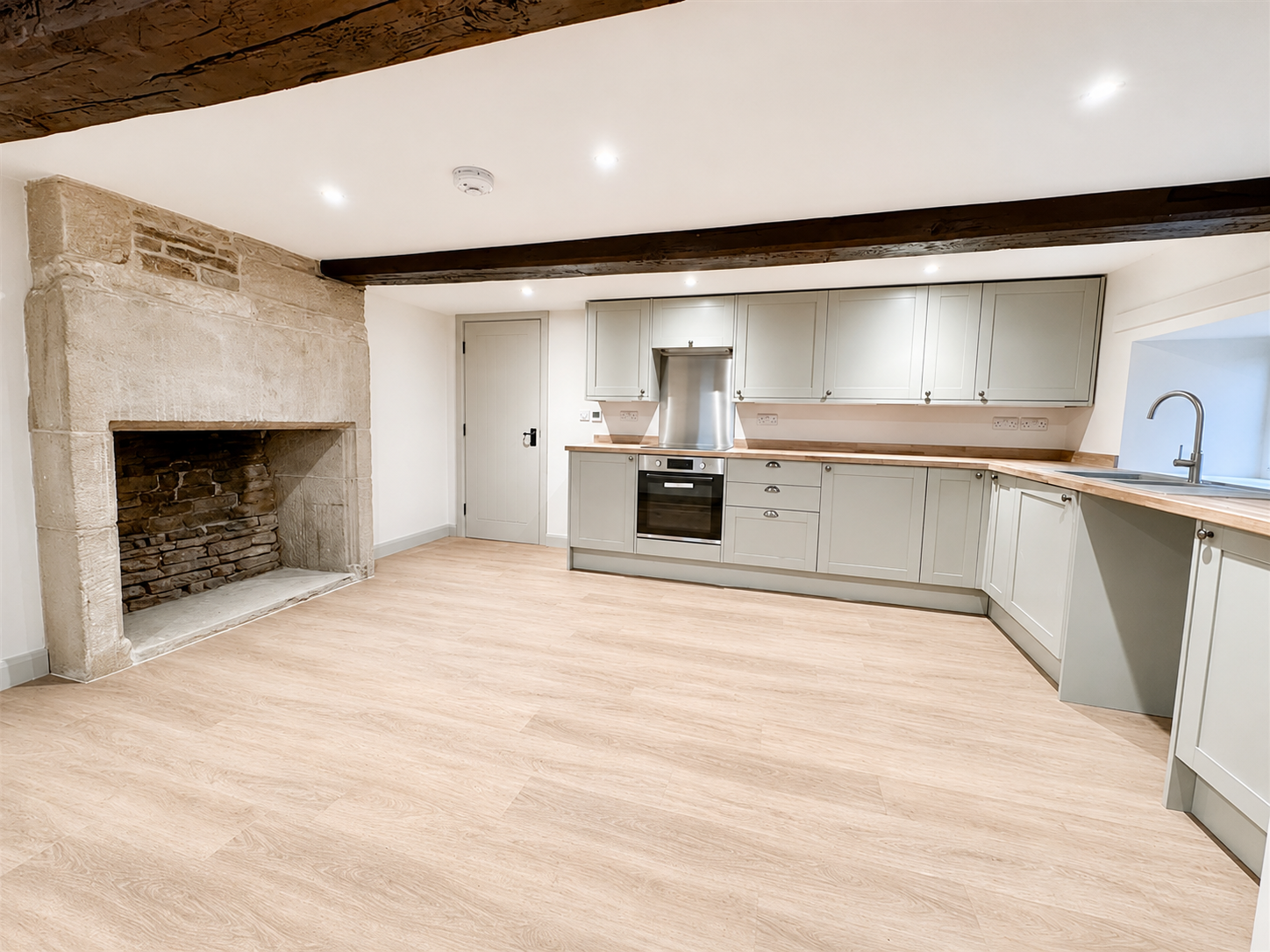 Renovated kitchen and living space within a traditional property featuring restored fireplace and exposed timber beams.