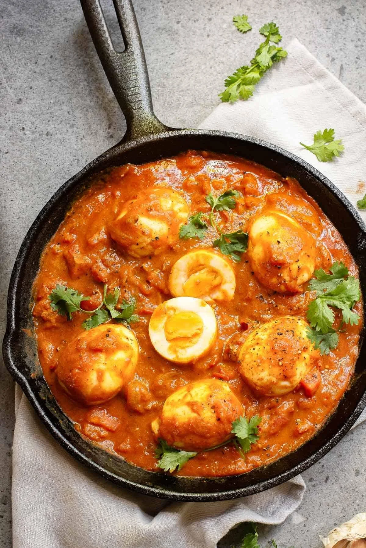 Shakshuka in a black skillet garnished with cilantro, on a light gray surface with a white napkin and cilantro sprigs nearby.