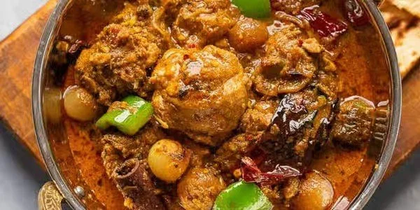 A bowl of spicy Indian curry with meat, vegetables, and spices.