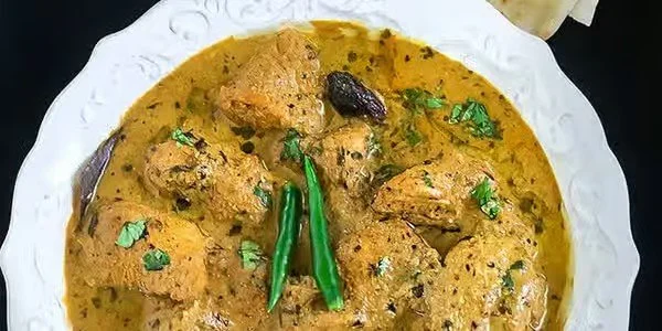 A white plate with chicken curry garnished with chopped cilantro and two green chili peppers.