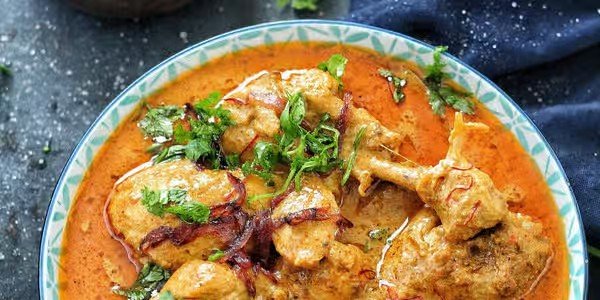 Close-up of a bowl of Indian chicken curry garnished with cilantro, served with a creamy sauce.