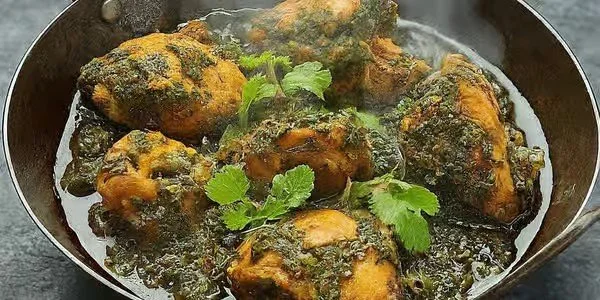 Close-up of cooked chicken with herbs and green garnish in a skillet.