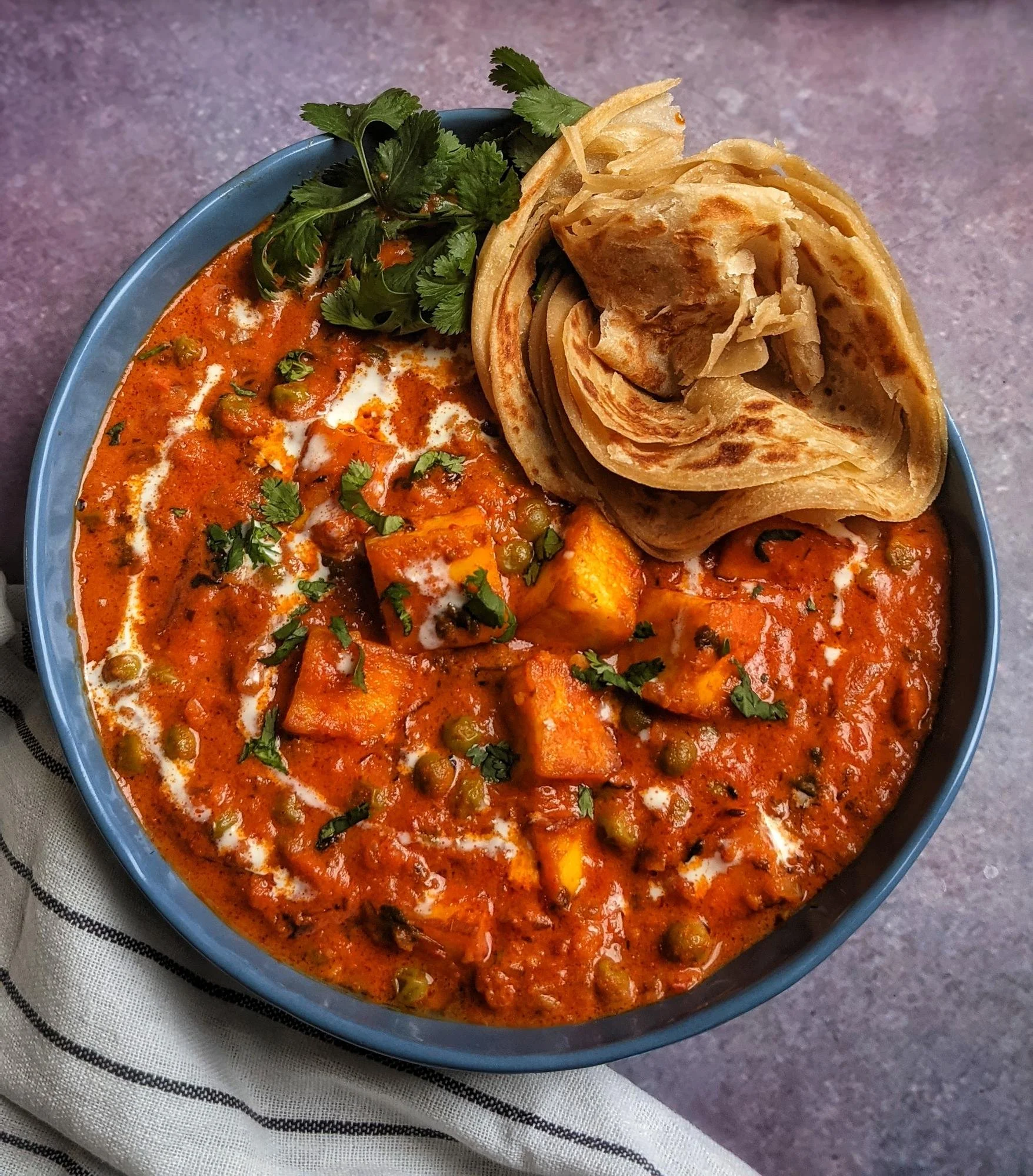 A bowl of Indian vegetable curry topped with cilantro and served with a side of Indian flatbread called paratha, on a cloth napkin.