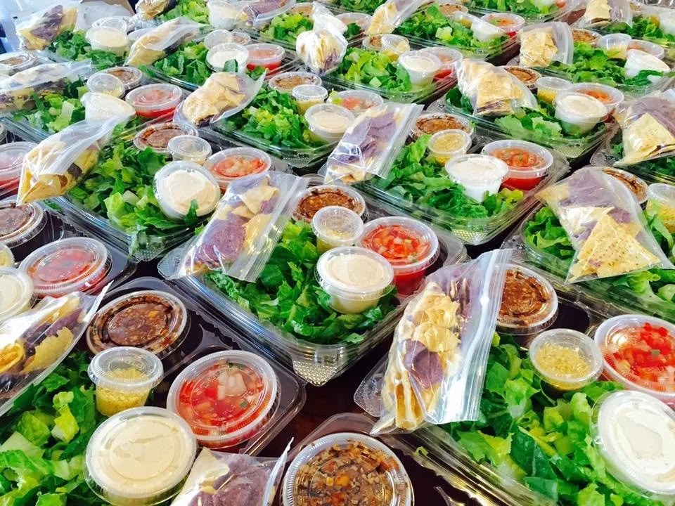 Multiple pre-packaged salads with lettuce, sliced tomatoes, and various sauces in small containers, some with plastic wrap.