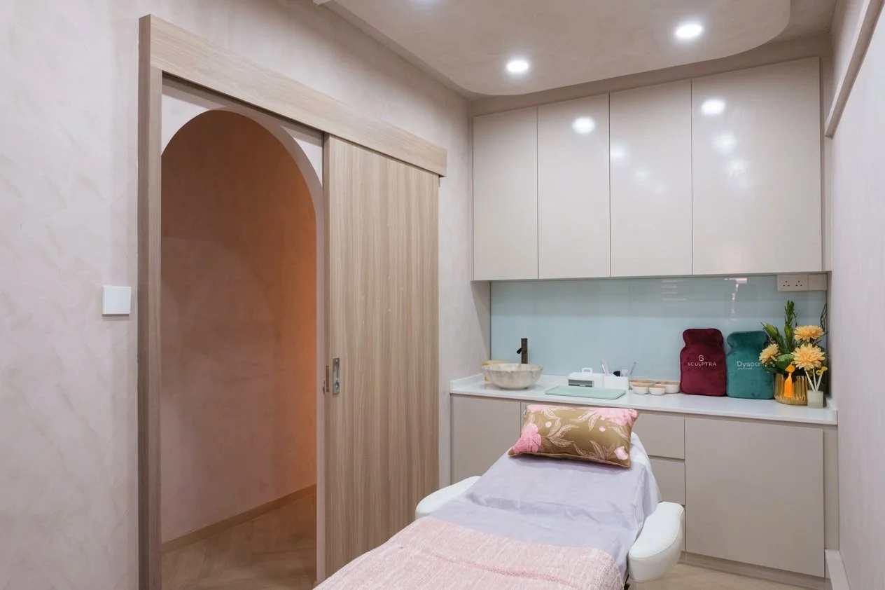 Medical room with treatment bed, beige walls, white cabinets, and a sliding wooden door, decorated with flowers and treatment supplies.