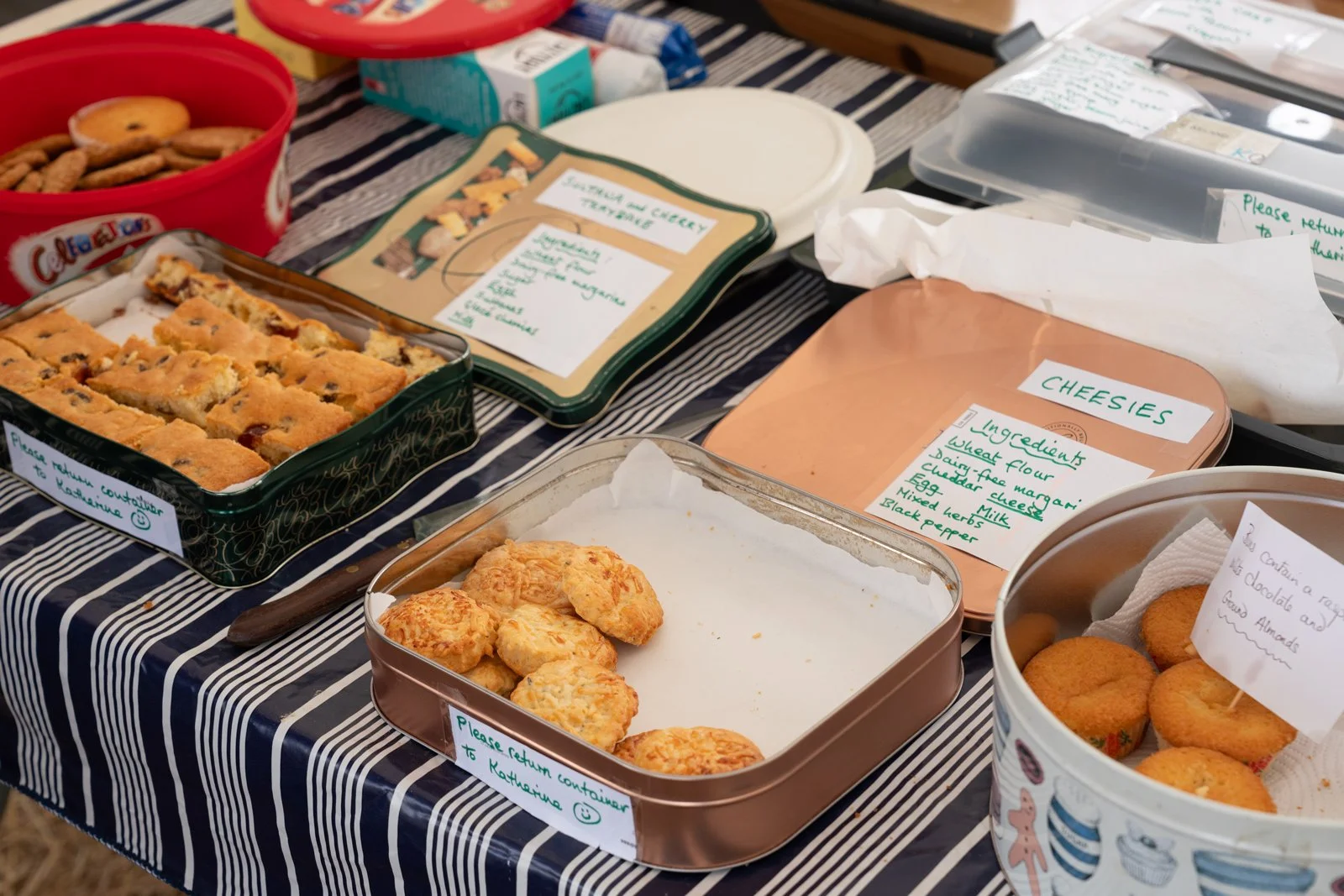 Assorted baked goods including cookies, scones, and a tray of cheese and vegetable quiche on a table with handwritten labels.