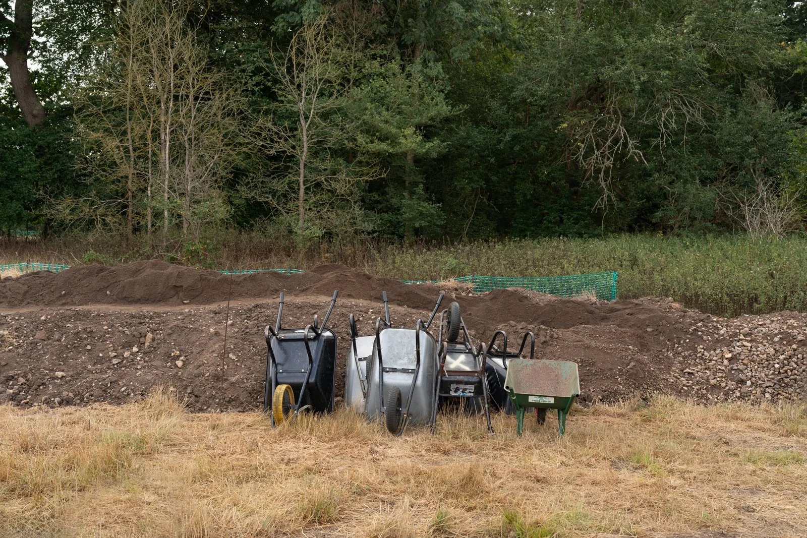 Construction site with dirt mounds, wheelbarrows, and a wheelbarrow among natural trees and vegetation