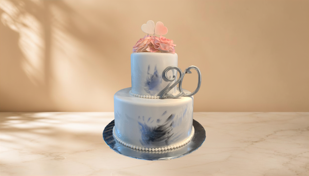 Two-tiered white and blue marbled cake with a silver "20" topper, pink flowers and heart decoration on top, sitting on a silver platter against a beige background with shadowed light.