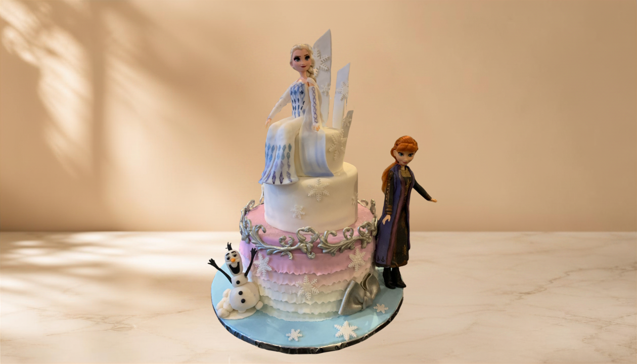 A two-tiered cake decorated with snowflakes, featuring figurines of Elsa, Anna, and Olaf from Frozen.