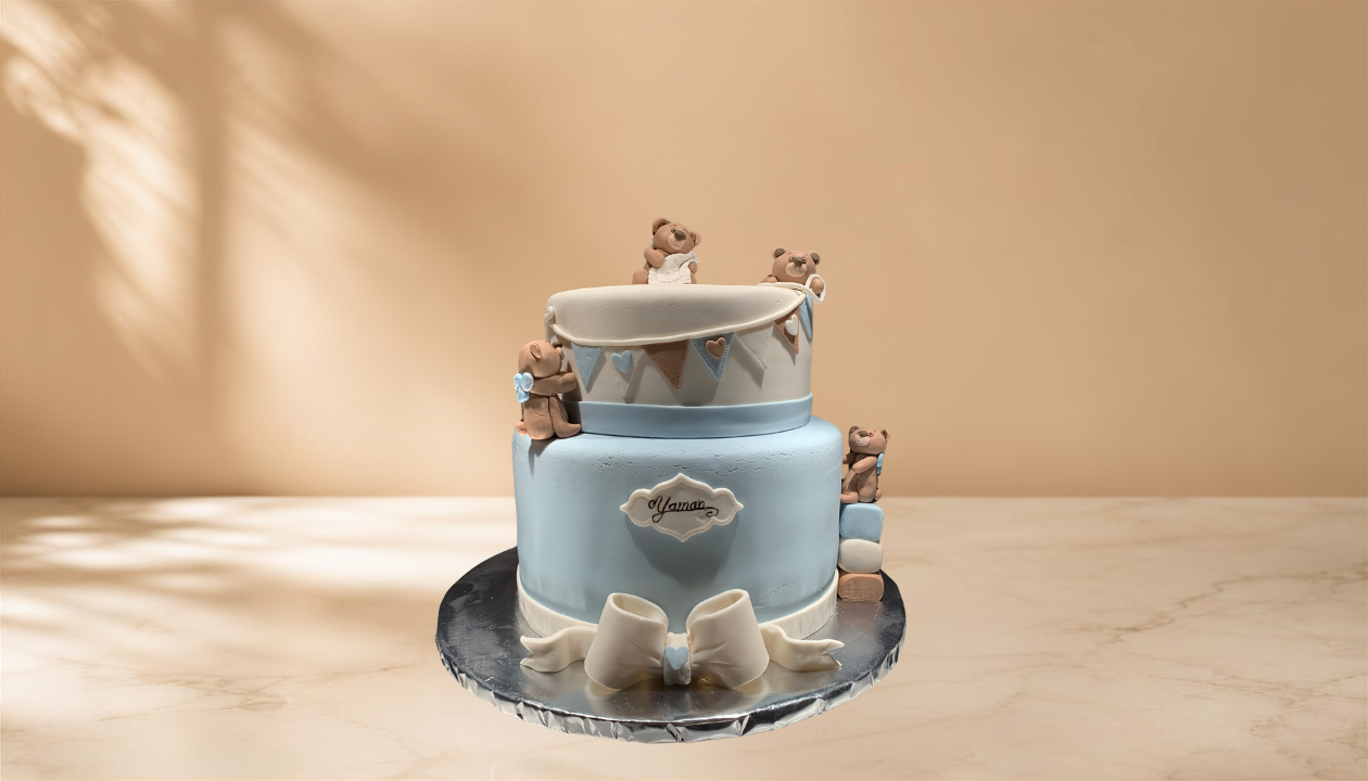 Two-tiered cake with blue and white fondant, decorated with small teddy bear figurines and a large bow on top, placed on a round silver cake board.