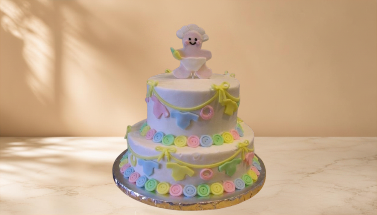 Two-tiered pastel-colored birthday cake decorated with fondant buttons, bows, and baby clothing items, topped with a cute lamb holding a spoon.