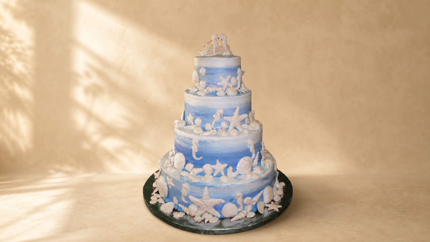 Four-tiered wedding cake decorated with white ocean-themed shells, starfish, and seahorses, featuring a blue and white marbled pattern.