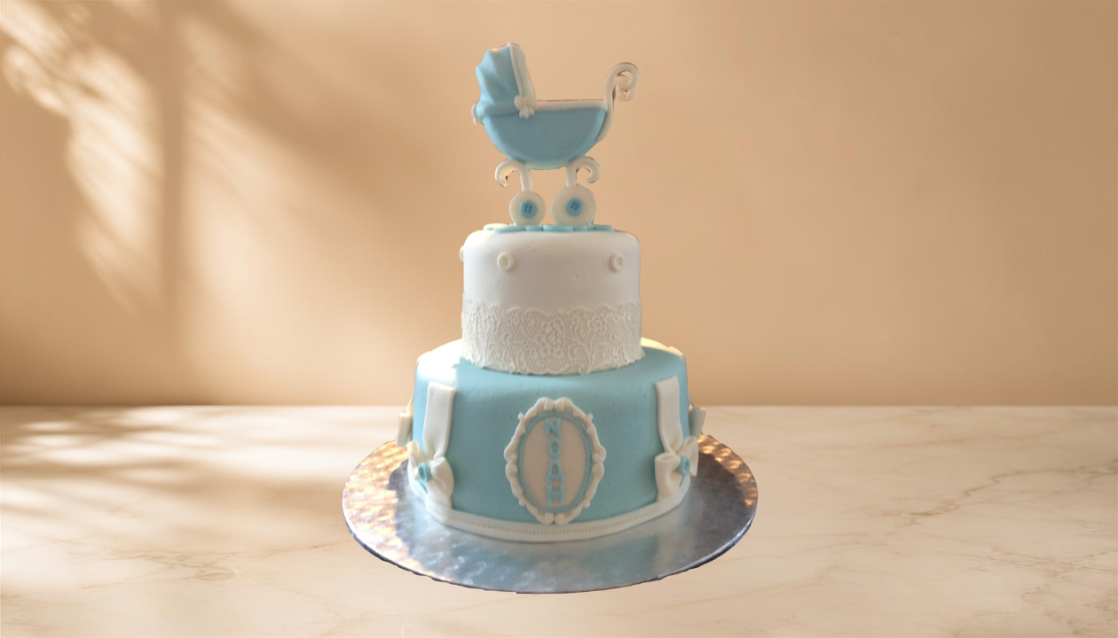 Two-tiered baby shower cake with white and light blue fondant, decorated with baby clothes and a baby stroller topper, on a silver cake board.