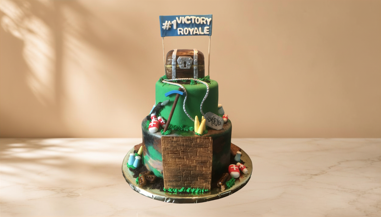 A two-tiered cake themed after the video game Fortnite, featuring a small treasure chest, a pickaxe, a gnome, and decorative items, with a blue flag reading '#1 Victory Royale' on top.