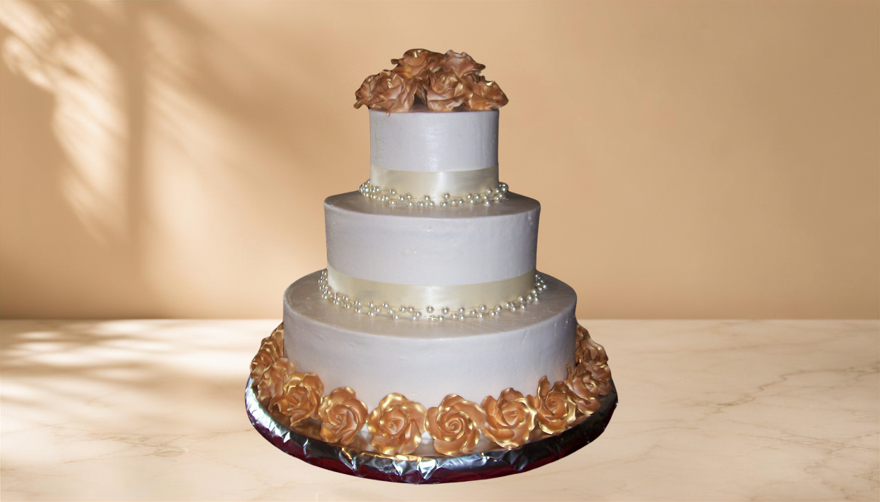 A three-tiered white wedding cake decorated with pearl-like beads, gold roses at the base and top, and a floral topper on the top tier, on a marble surface with a beige background.