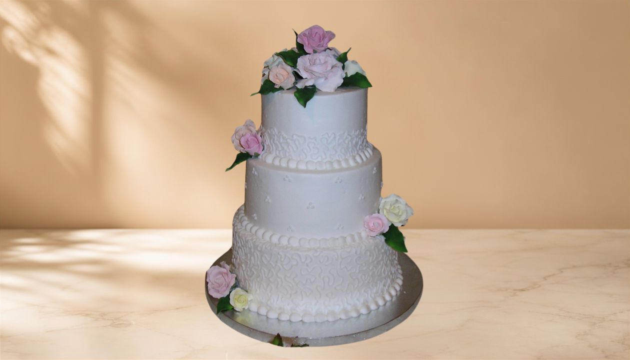 White three-tier wedding cake decorated with pink and white flowers on a silver platter against a beige background.