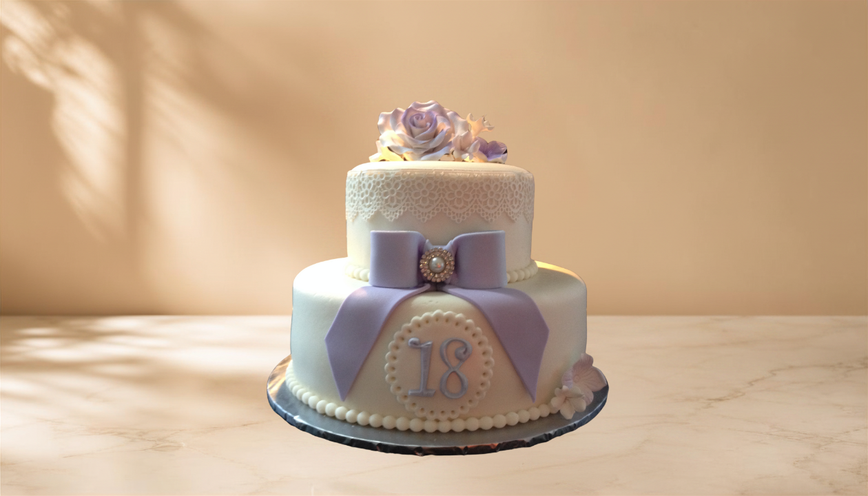 A two-tiered white birthday cake decorated with a lavender bow, pearl accents, and a sugar flower topper, with the number 18 on the front, placed on a marble surface.