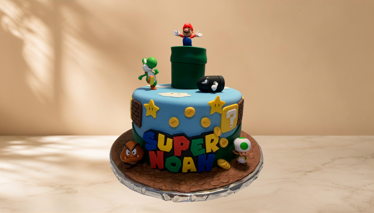 A birthday cake decorated with Super Mario characters and elements. The cake features figurines of Mario, Yoshi, Toad, and a Goomba, along with themed decorations like question marks and star symbols, and the words "Super Noah" in colorful letters.