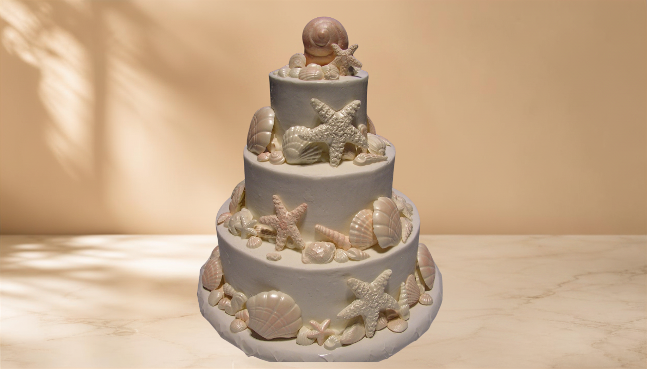 Three-tiered white cake decorated with seashells and starfish made of fondant or icing, featuring a seashell topper on top.