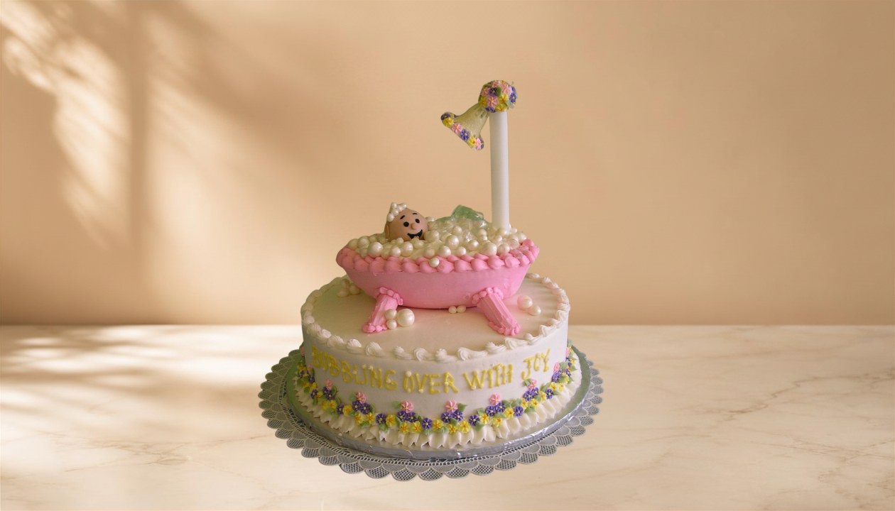 A birthday cake with a baby in a bathtub topper, decorated with white, pink, yellow, purple, and green fondant and icing, with the message "BUBBLING OVER WITH JOY" on the side.