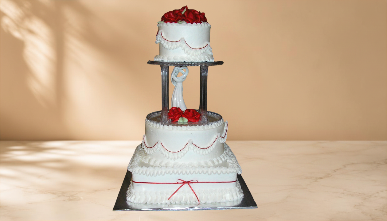A three-tiered white wedding cake with red roses and decorative piping, displayed on a black and silver cake stand