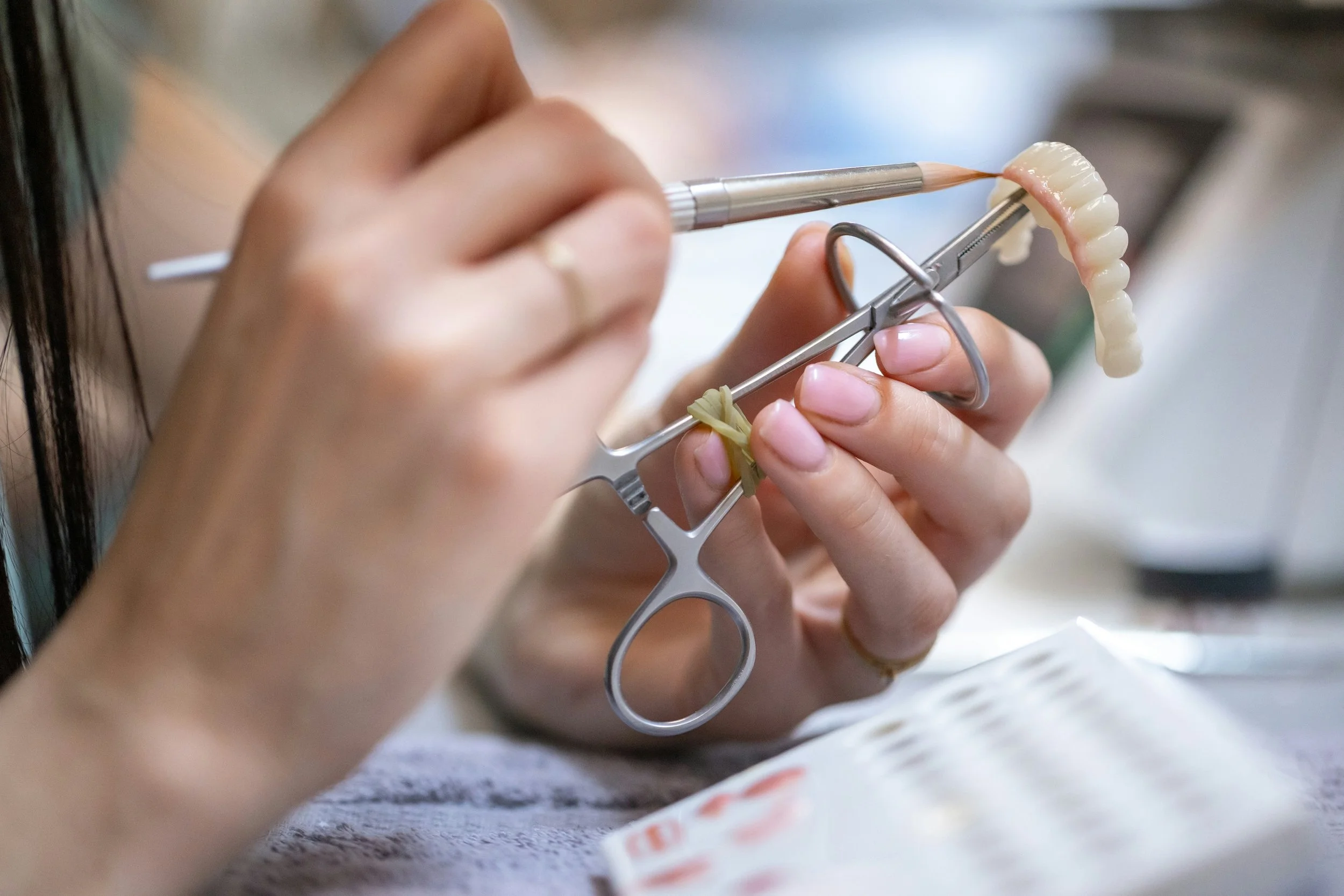 Close-up of a dental technician shaping a dental prosthetic using a precision tool, with a dental model held in place.