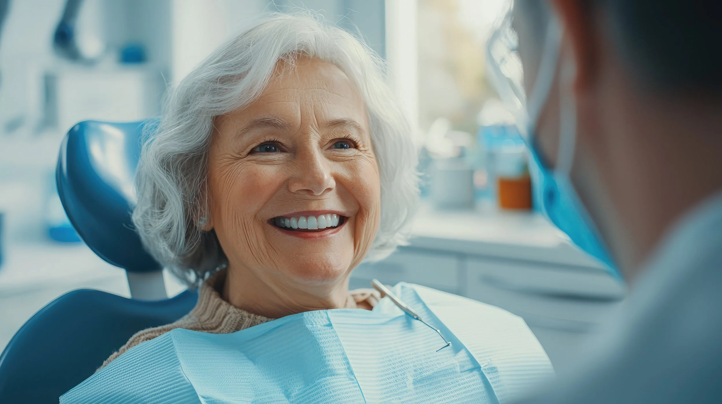 An elderly woman with white hair smiling at a dentist in a dental clinic.
