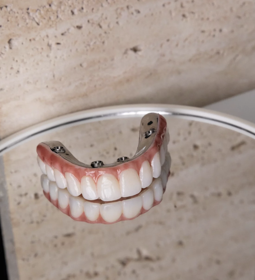 A set of removable dentures resting on a round mirror with a beige textured background.